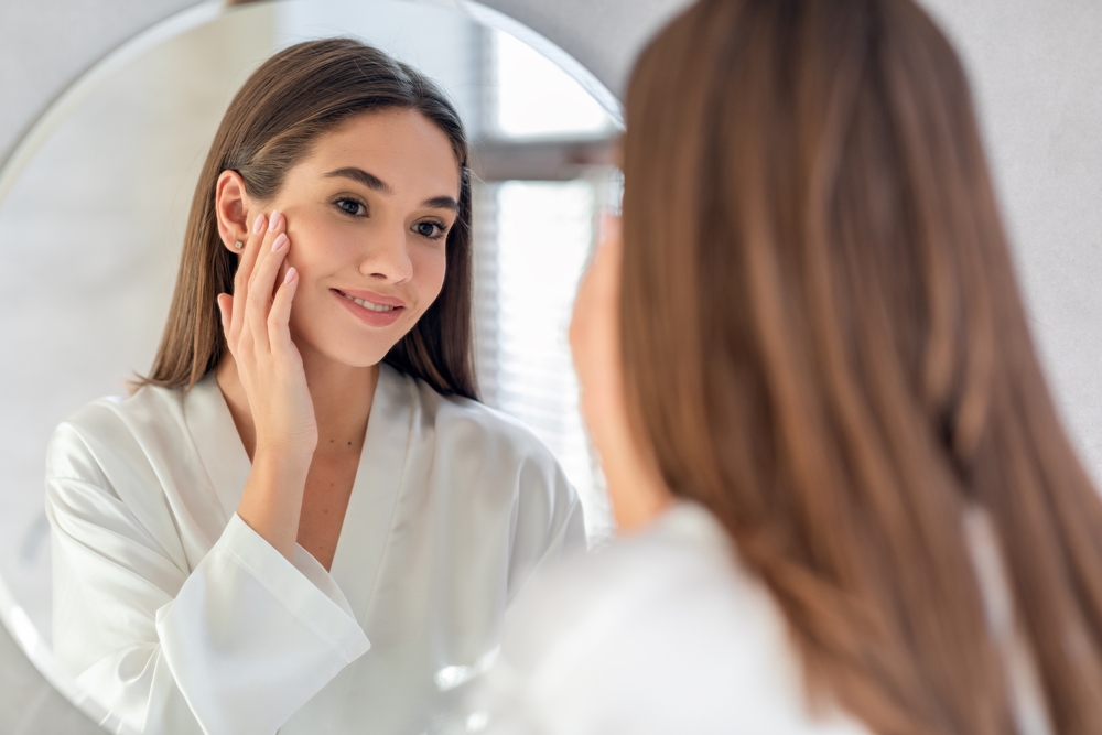 Woman smiling in the mirror after receiving Acne Facials